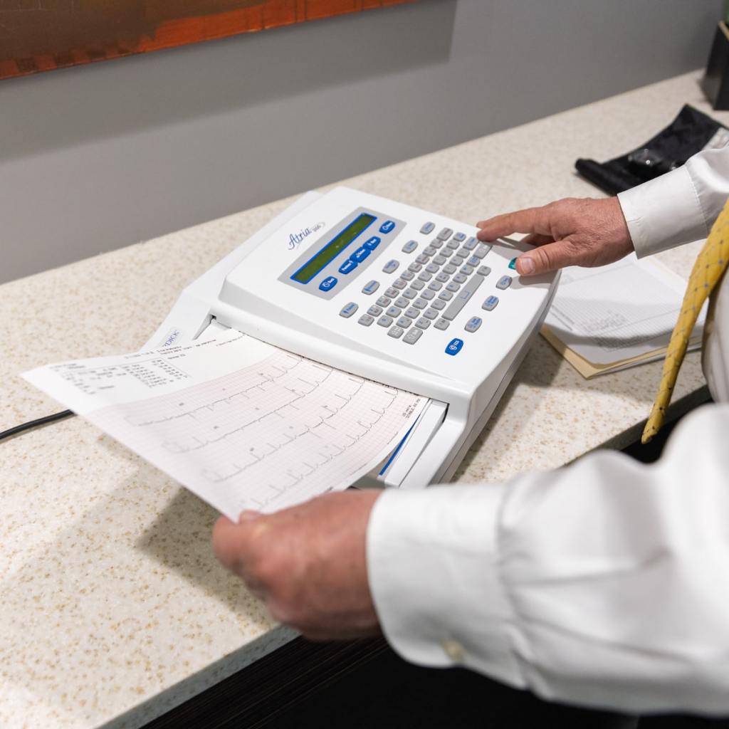 Close-up of a doctor’s hands reviewing an EKG printout from the machine during a pilot's medical exam.