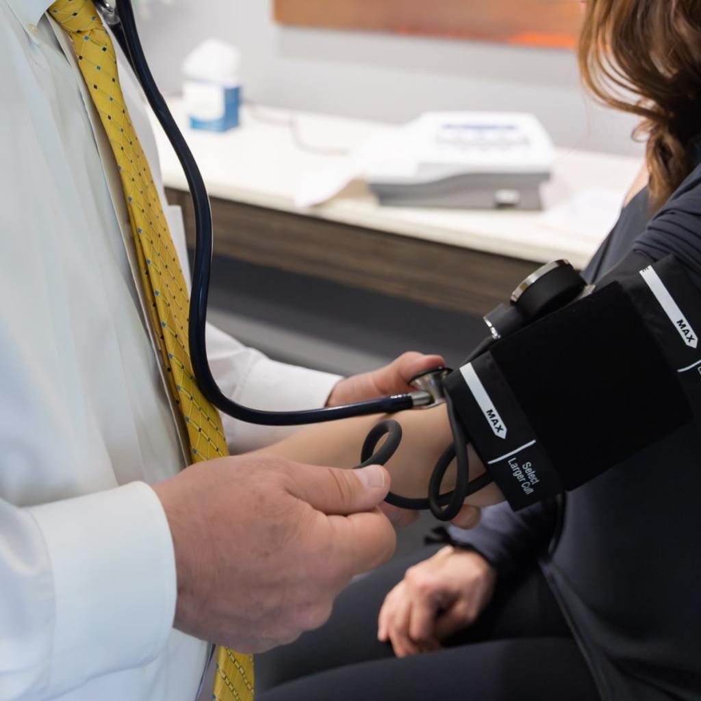 Doctor taking a female pilot’s blood pressure on a medical exam table, addressing complex medical needs.